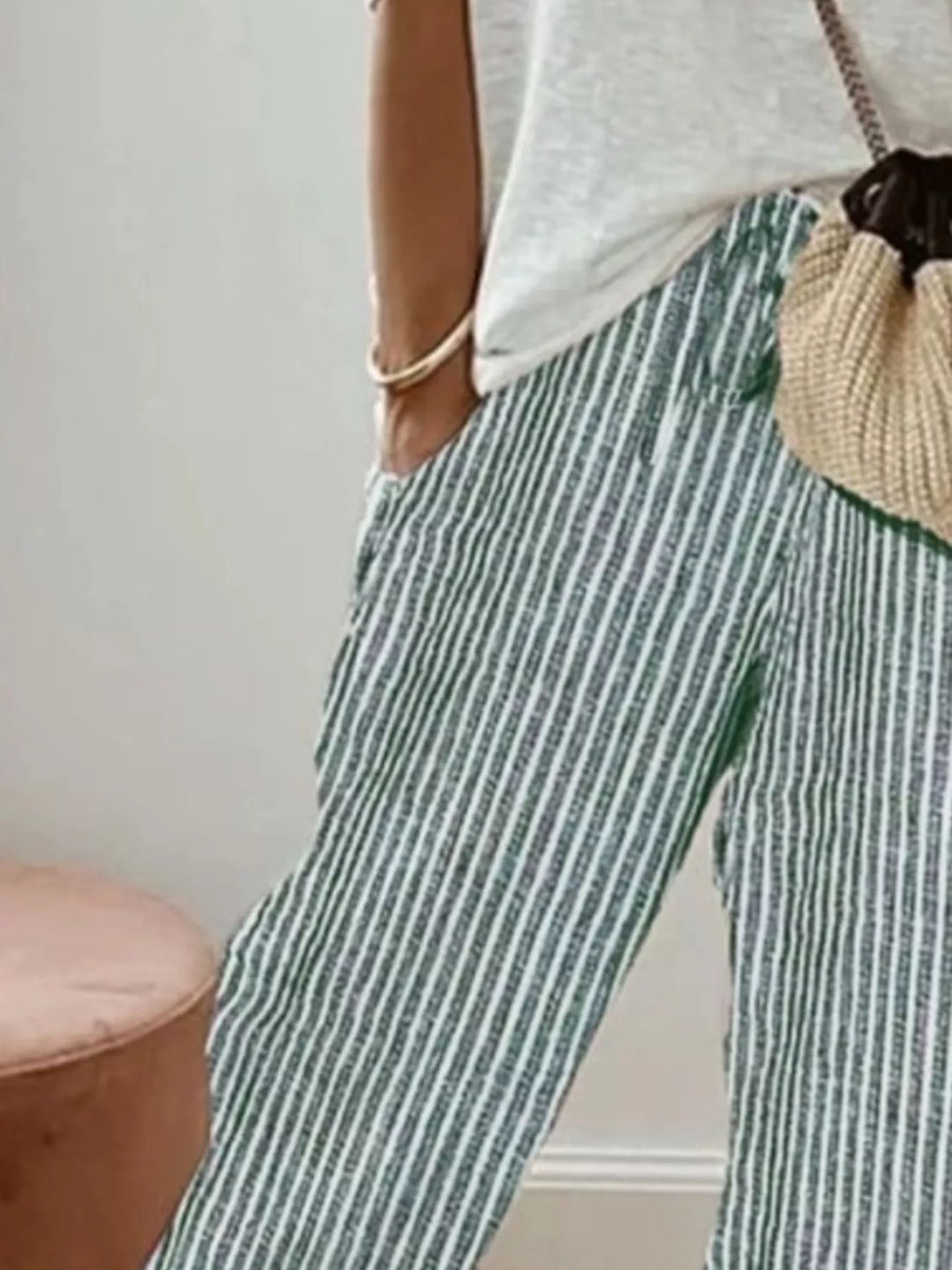Person wearing green and white striped pants with a neutral-colored bag.