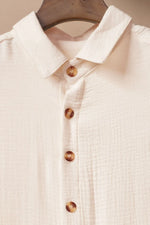 Close-up of a cream-colored shirt with wooden buttons on a beige background