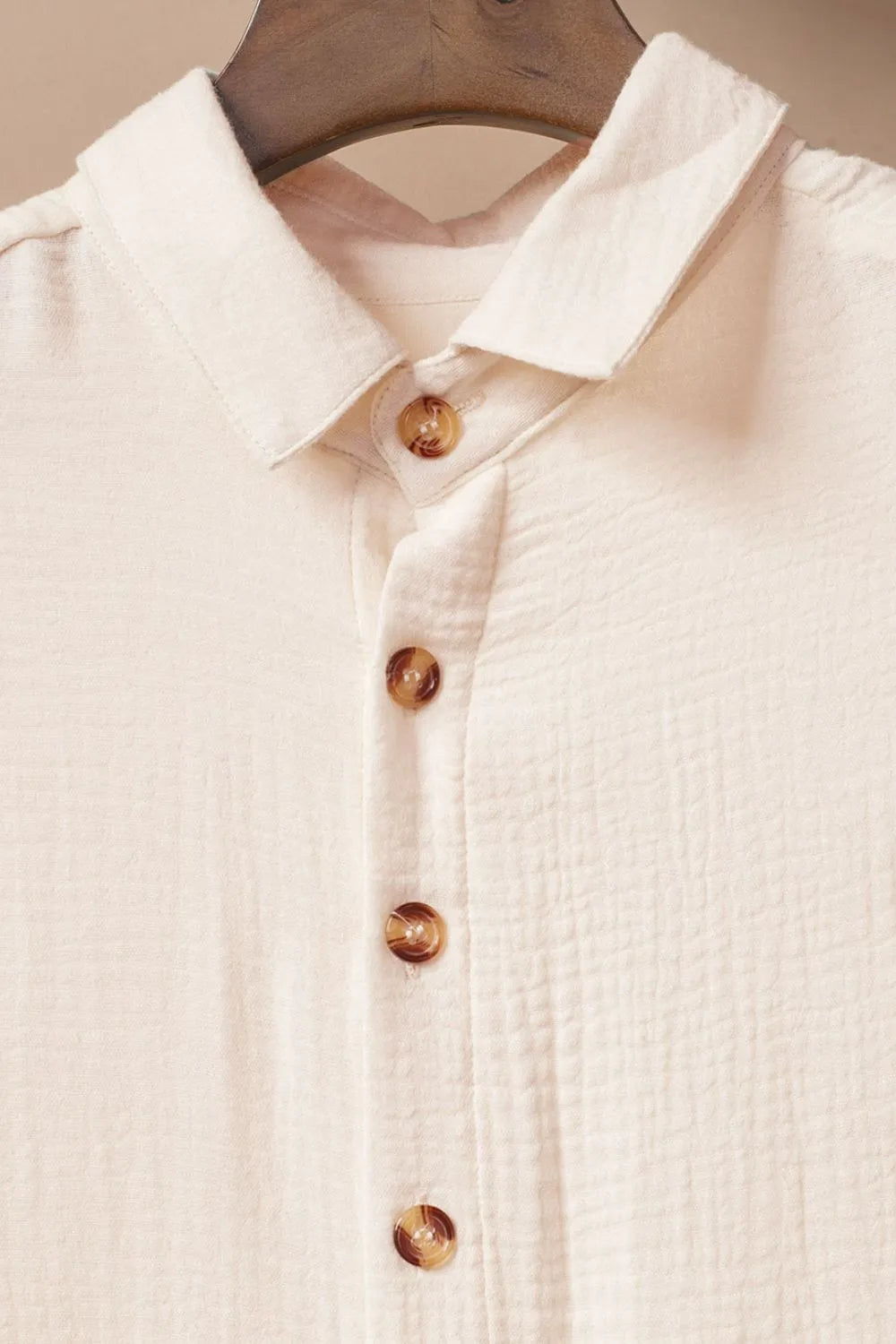 Close-up of a cream-colored shirt with wooden buttons on a beige background