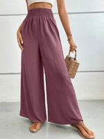 Person wearing mauve wide-leg pants with a white top and brown sandals on a light gray background