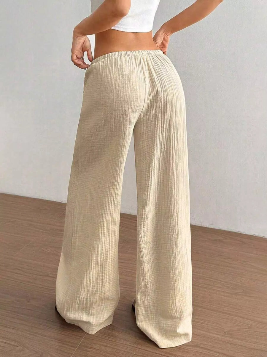 Beige wide-leg pants worn by a person on a wooden floor with a white wall background