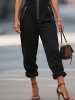 Person wearing black pants with gold zippers, holding a brown handbag on a blurred background
