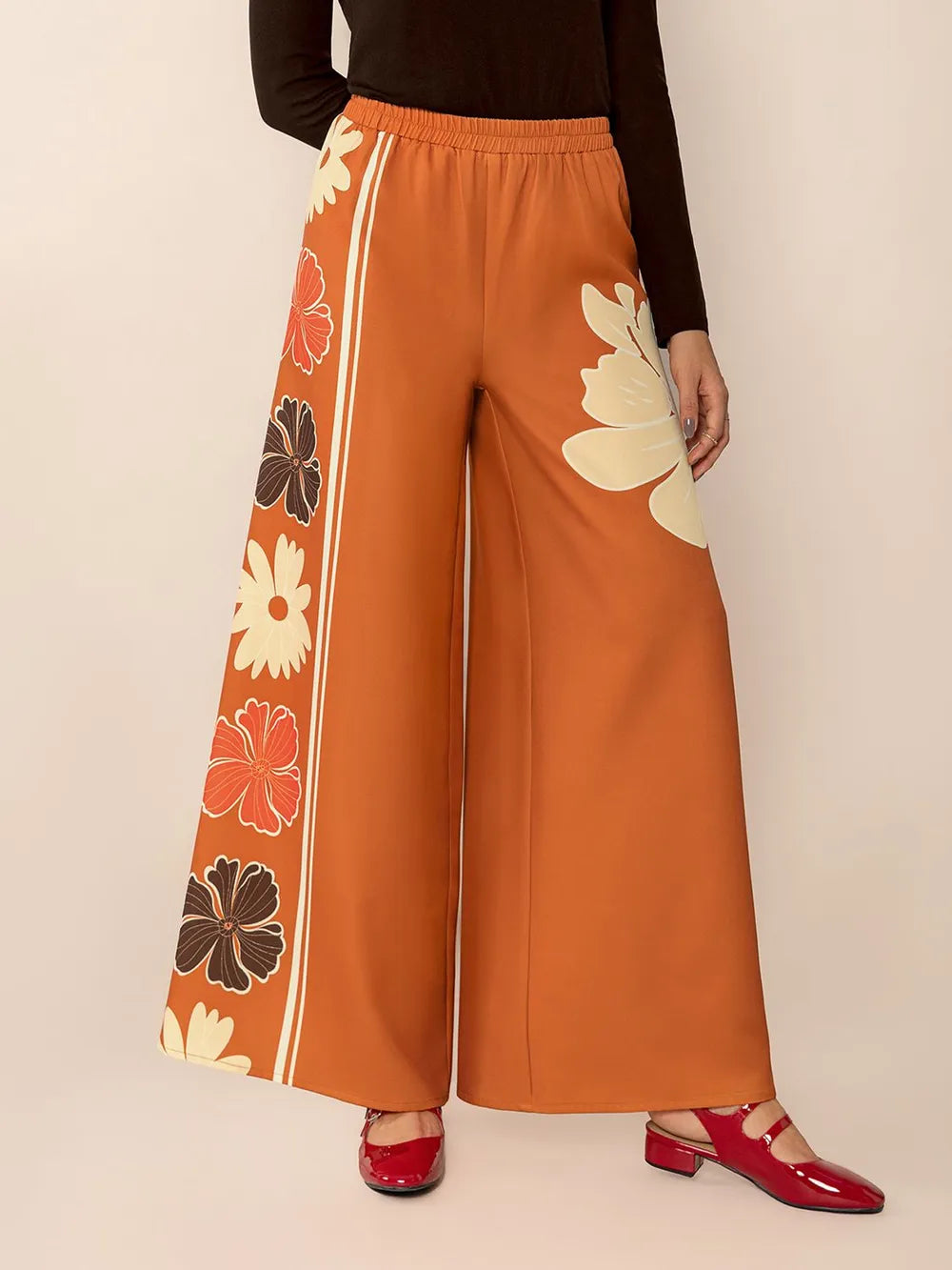 Orange wide-leg pants with floral patterns on a beige background