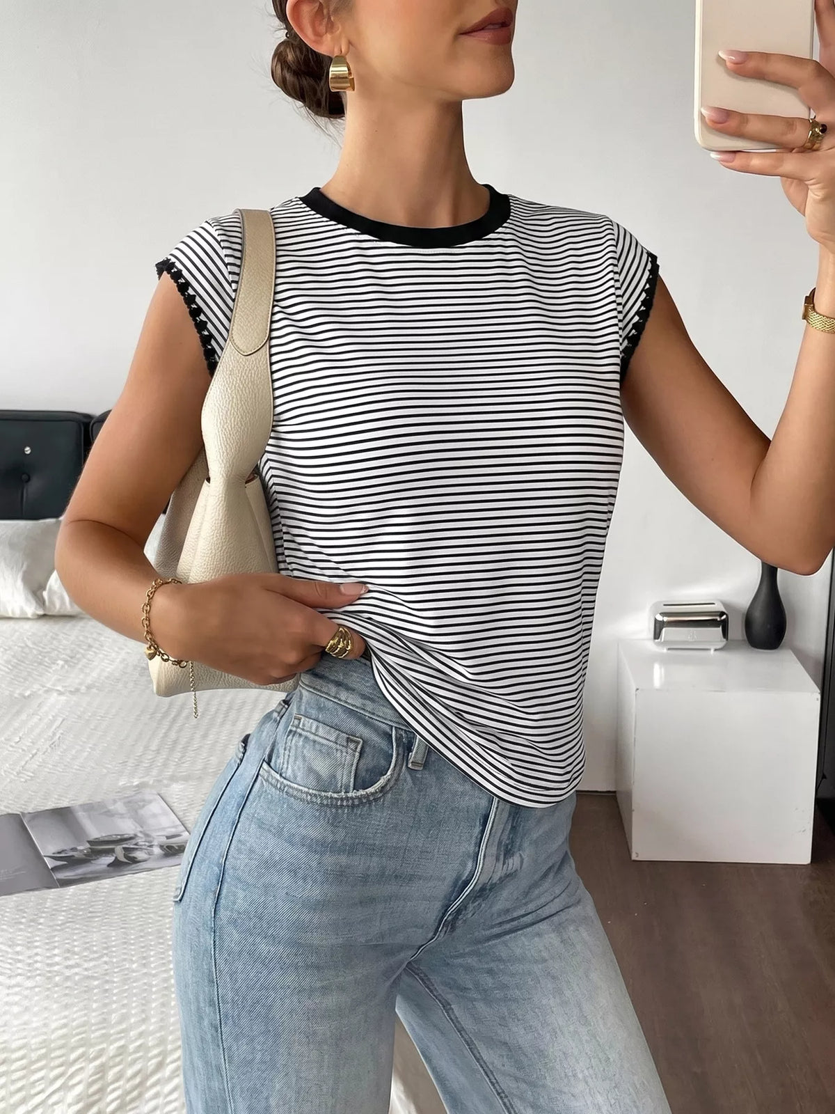 Person wearing a black and white striped shirt and light blue jeans, taking a mirror selfie.