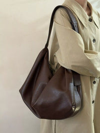 Person wearing a brown leather bag over one shoulder against a plain background
