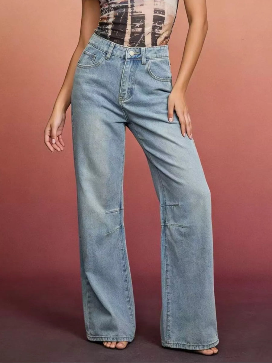 Person wearing light blue flared jeans against a pinkish-brown background