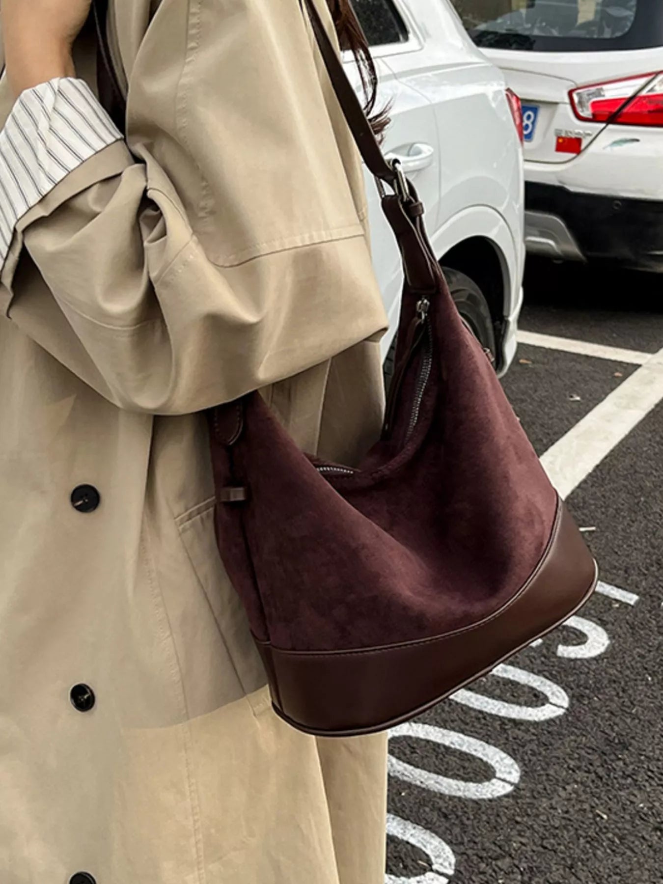 Person wearing a beige coat holding a brown handbag on a street.