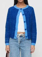 Person wearing a blue cardigan over a white top and jeans on a plain background