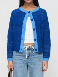 Person wearing a blue cardigan over a white top and jeans on a plain background