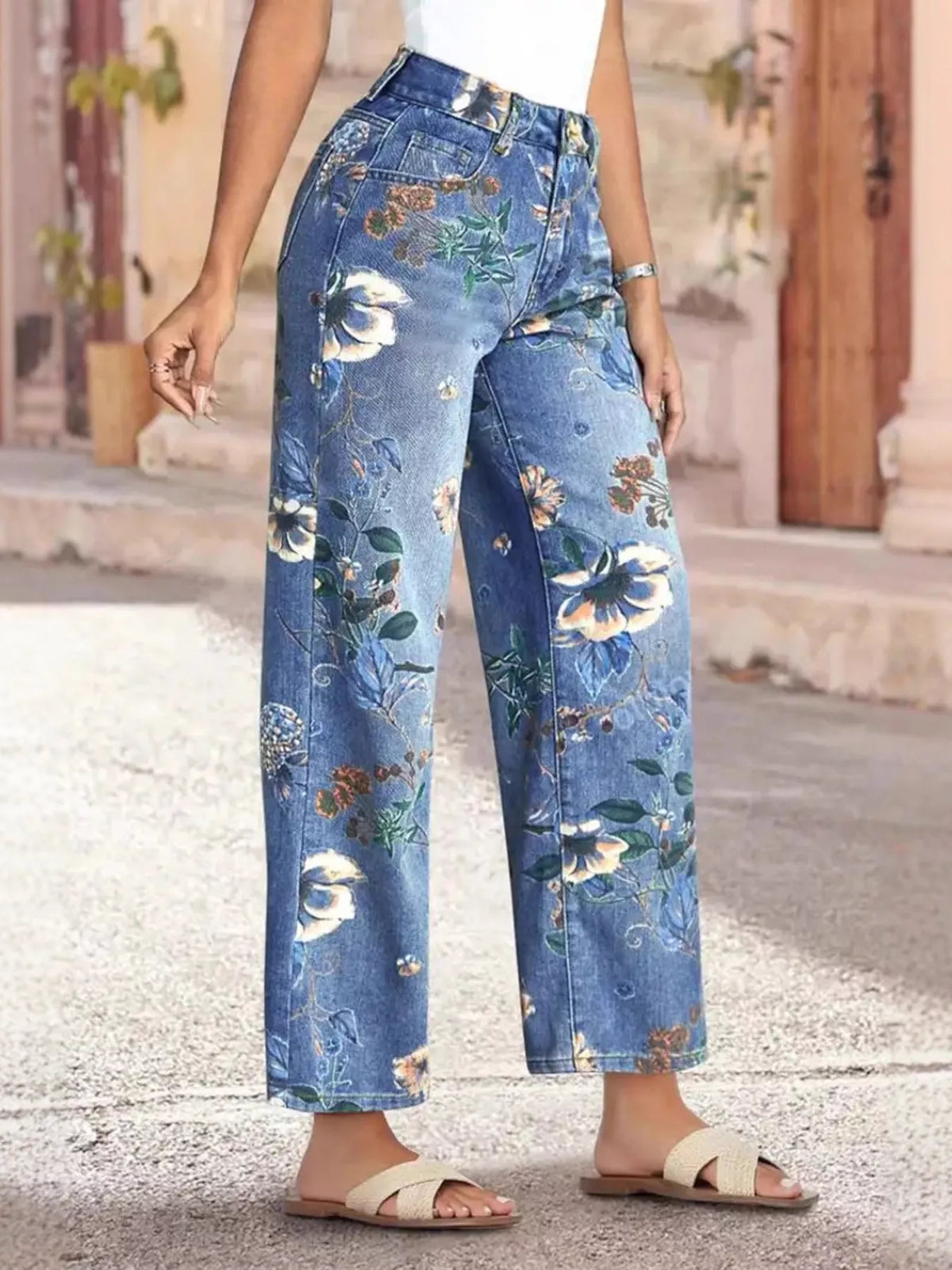 Person wearing floral-patterned blue jeans standing on a stone pavement.