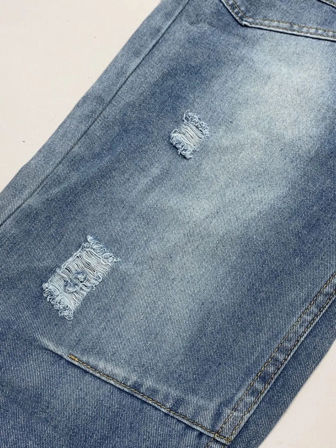 Close-up of a blue denim jacket with distressed details on a beige background