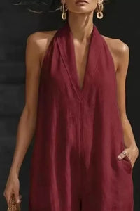 Woman wearing a burgundy halter neck jumpsuit against a black background