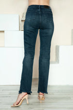 Person wearing dark blue jeans standing on a light wooden floor with a neutral-colored wall in the background.