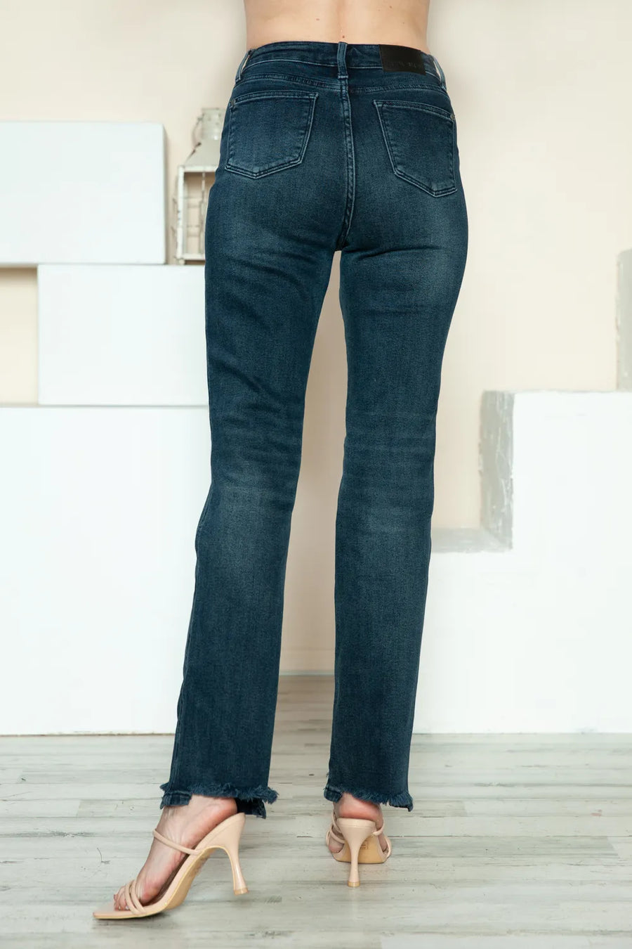 Person wearing dark blue jeans standing on a light wooden floor with a neutral-colored wall in the background.