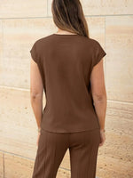 Woman wearing a brown outfit against a beige stone wall.