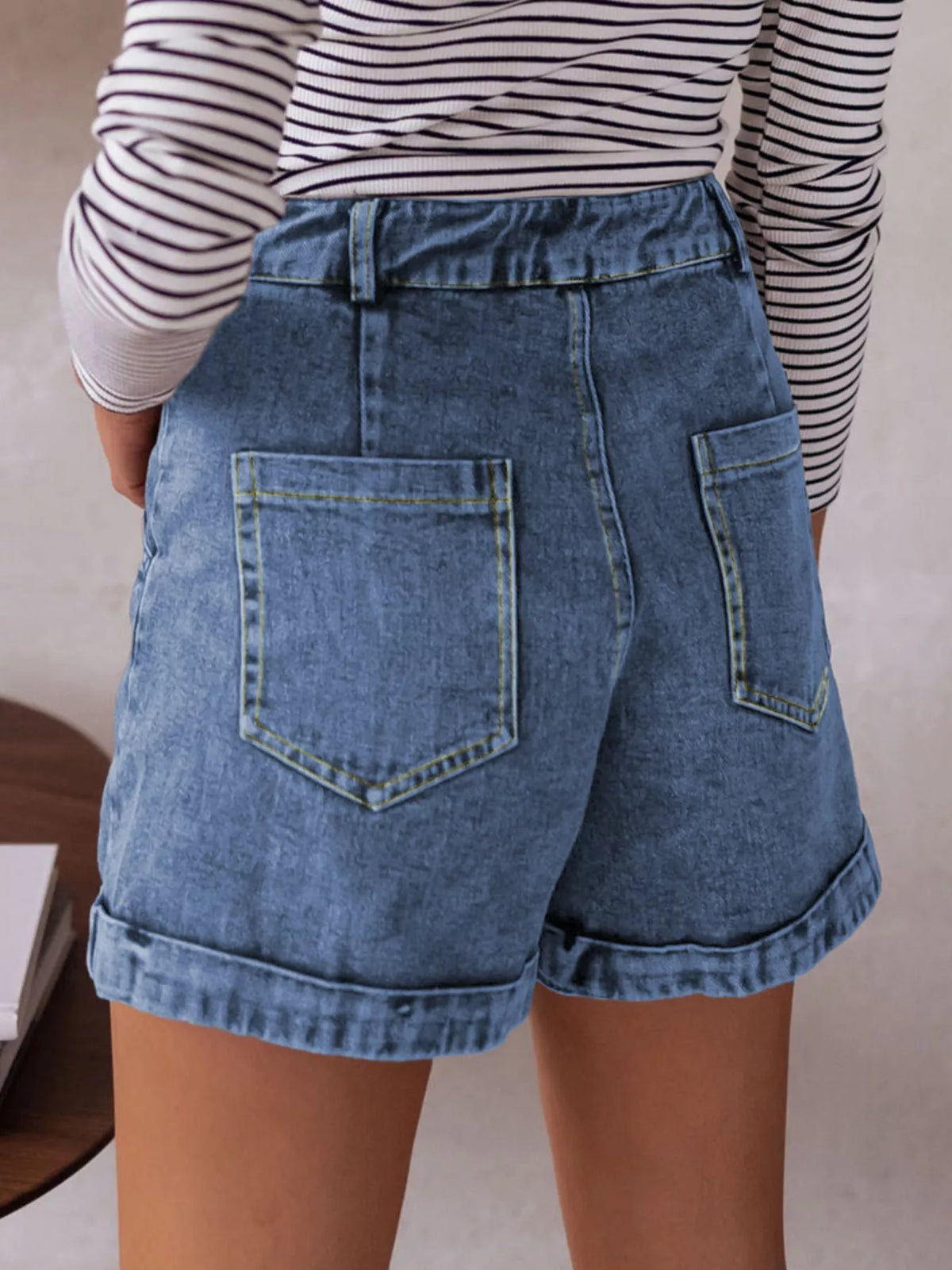 Person wearing blue denim shorts and a striped shirt against a neutral background