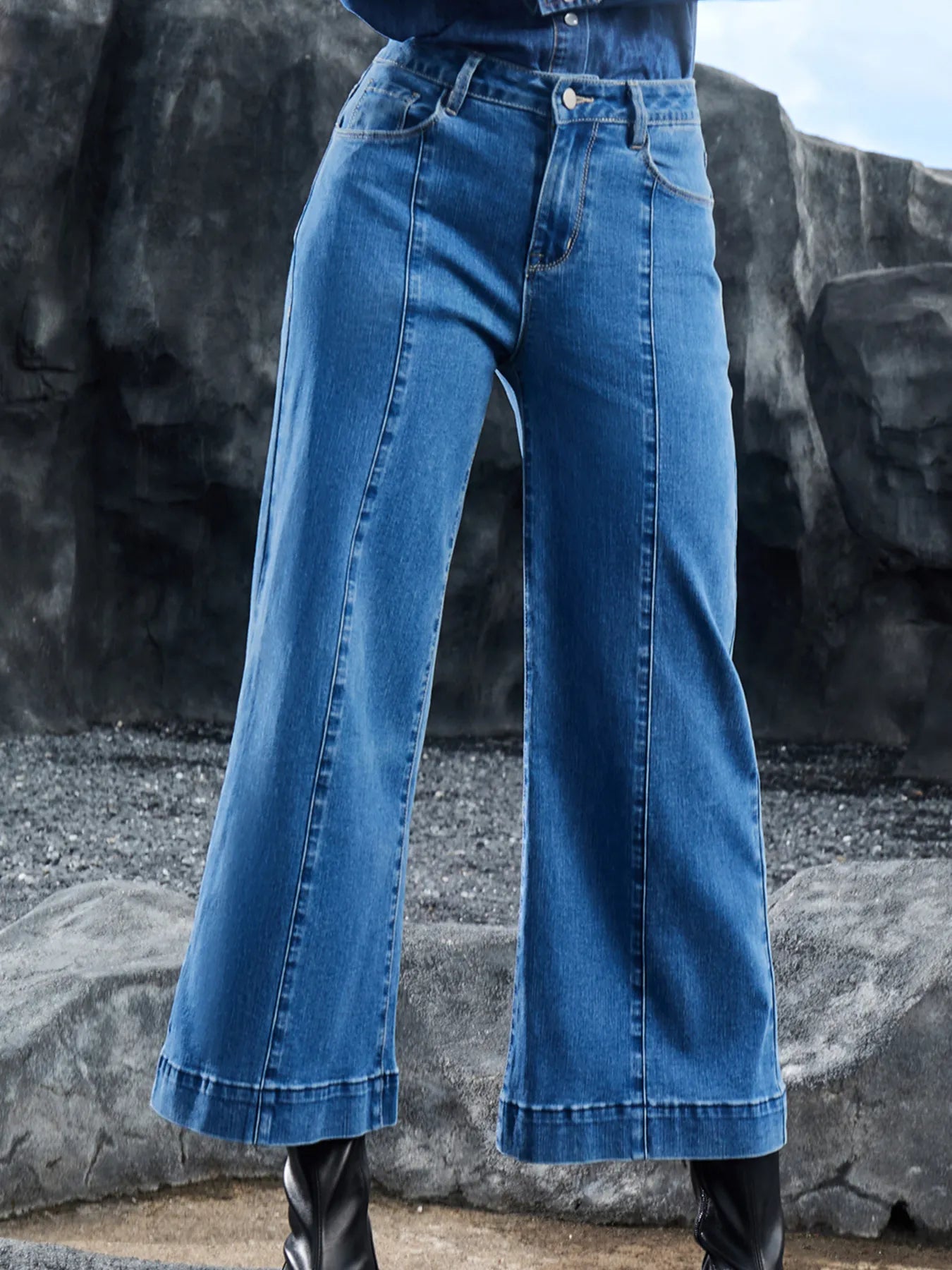 Wide-leg blue jeans worn by a person against a rocky background