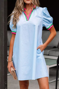 Woman wearing a light blue dress with pink and green trim, standing outdoors.