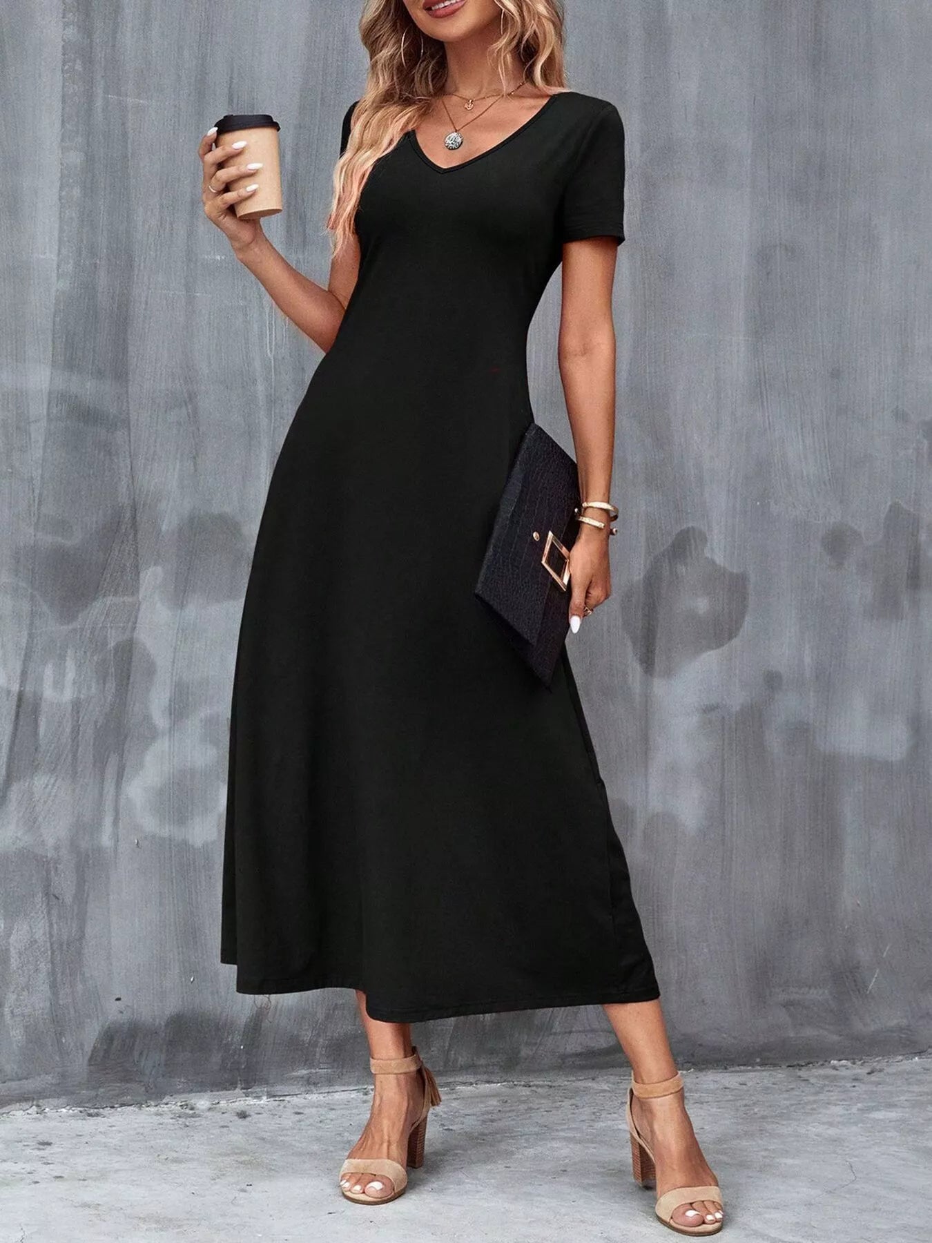Woman wearing a black dress holding a coffee cup against a gray wall.