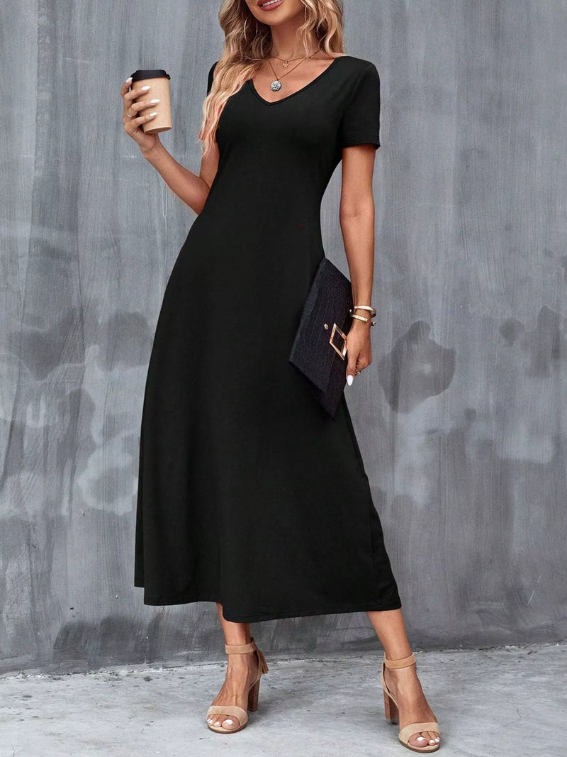 Woman wearing a black dress holding a coffee cup against a gray wall.