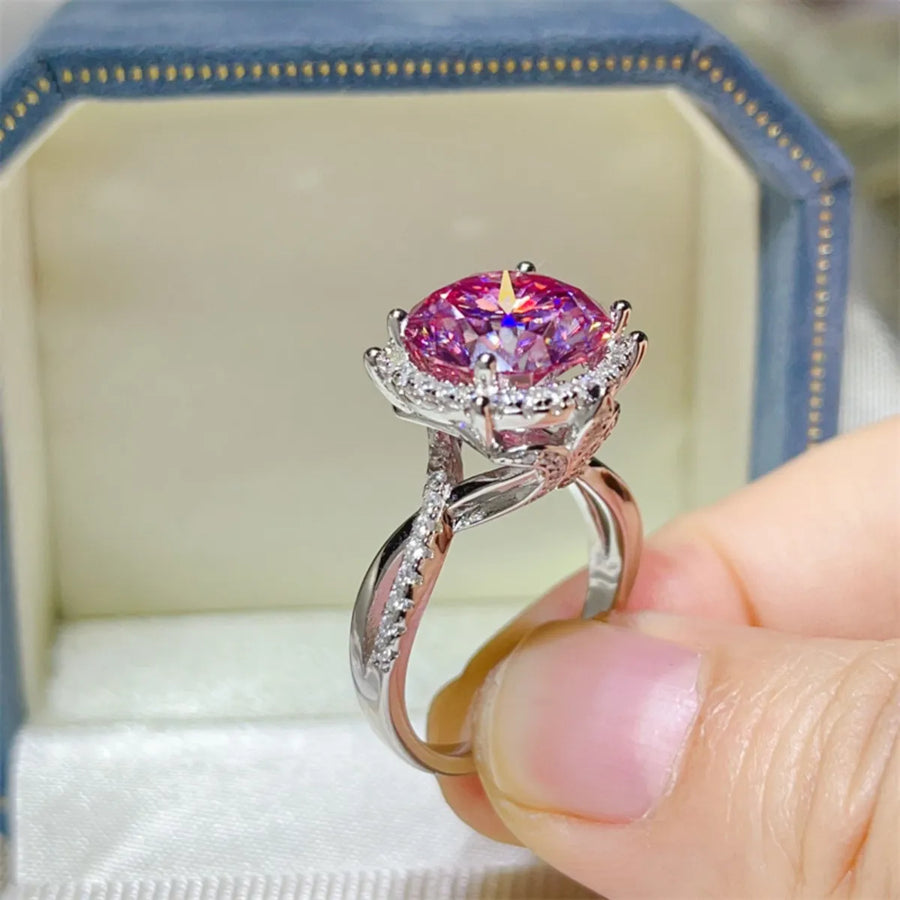 Pink gemstone ring with silver band held by a hand, displayed in a jewelry box.