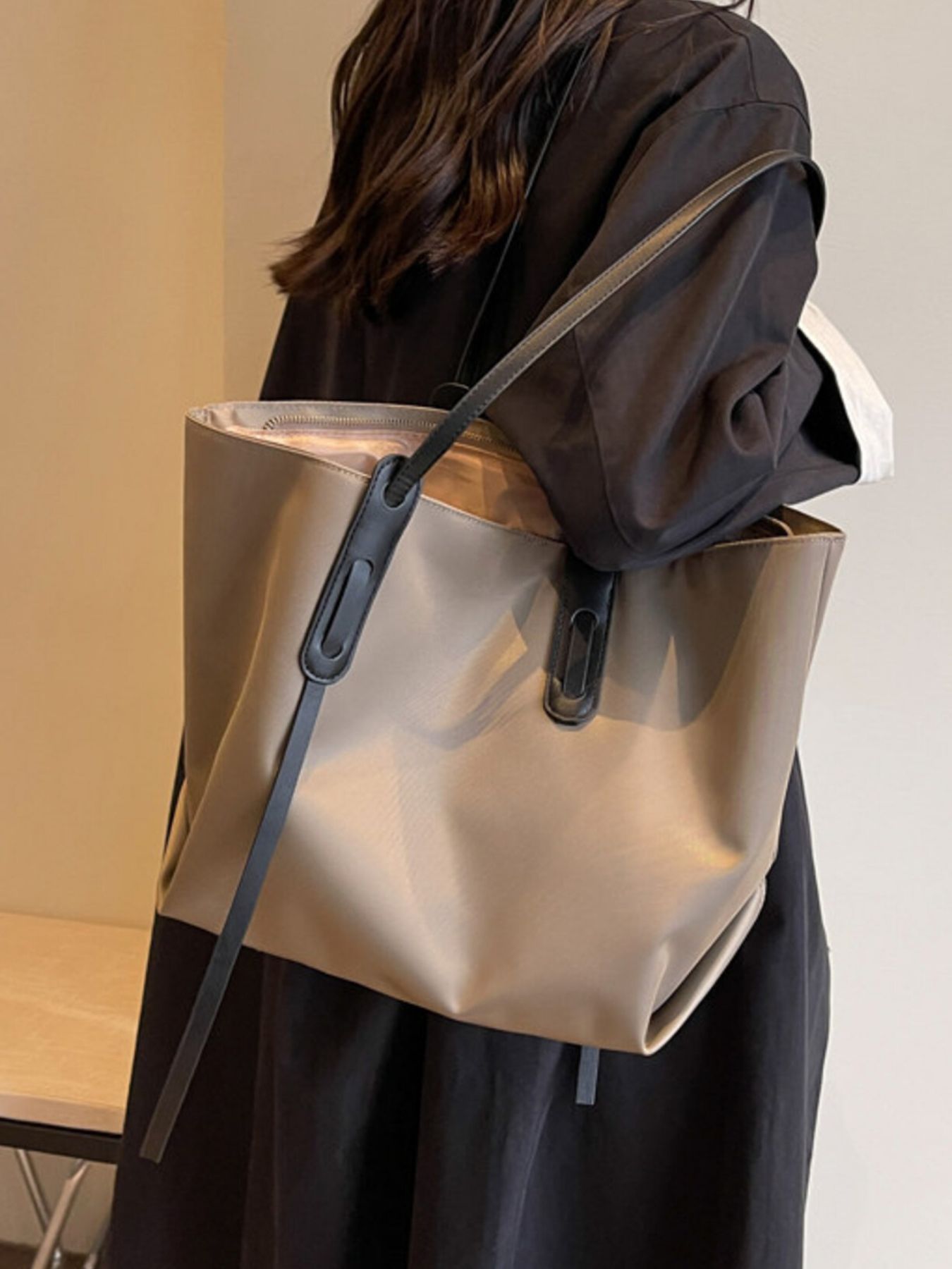 Person wearing a beige tote bag with a black strap on a neutral background