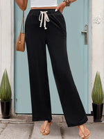 Person wearing black wide-leg pants with a white top and sandals, standing in front of a light blue door.