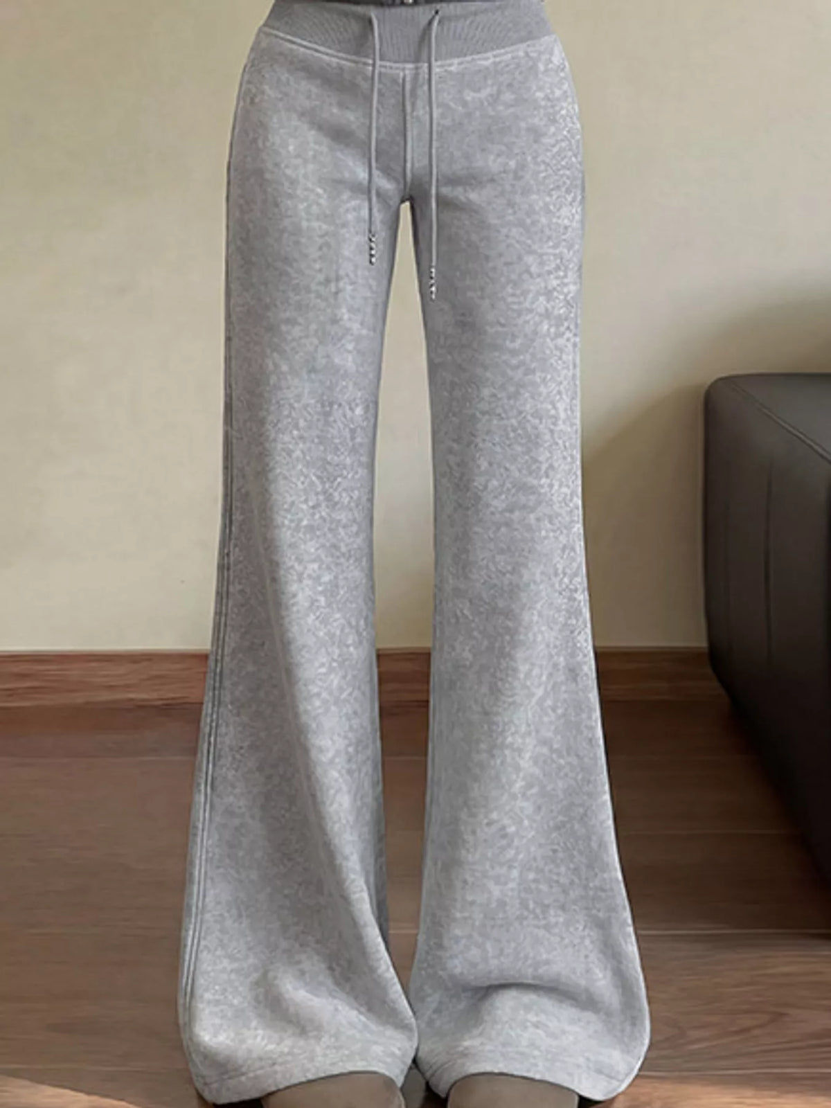 Light gray wide-leg sweatpants with a drawstring waist, shown on a model standing indoors on a wooden floor.