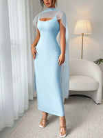 Woman wearing a light blue dress with sheer sleeves in a room with white curtains and a lamp.