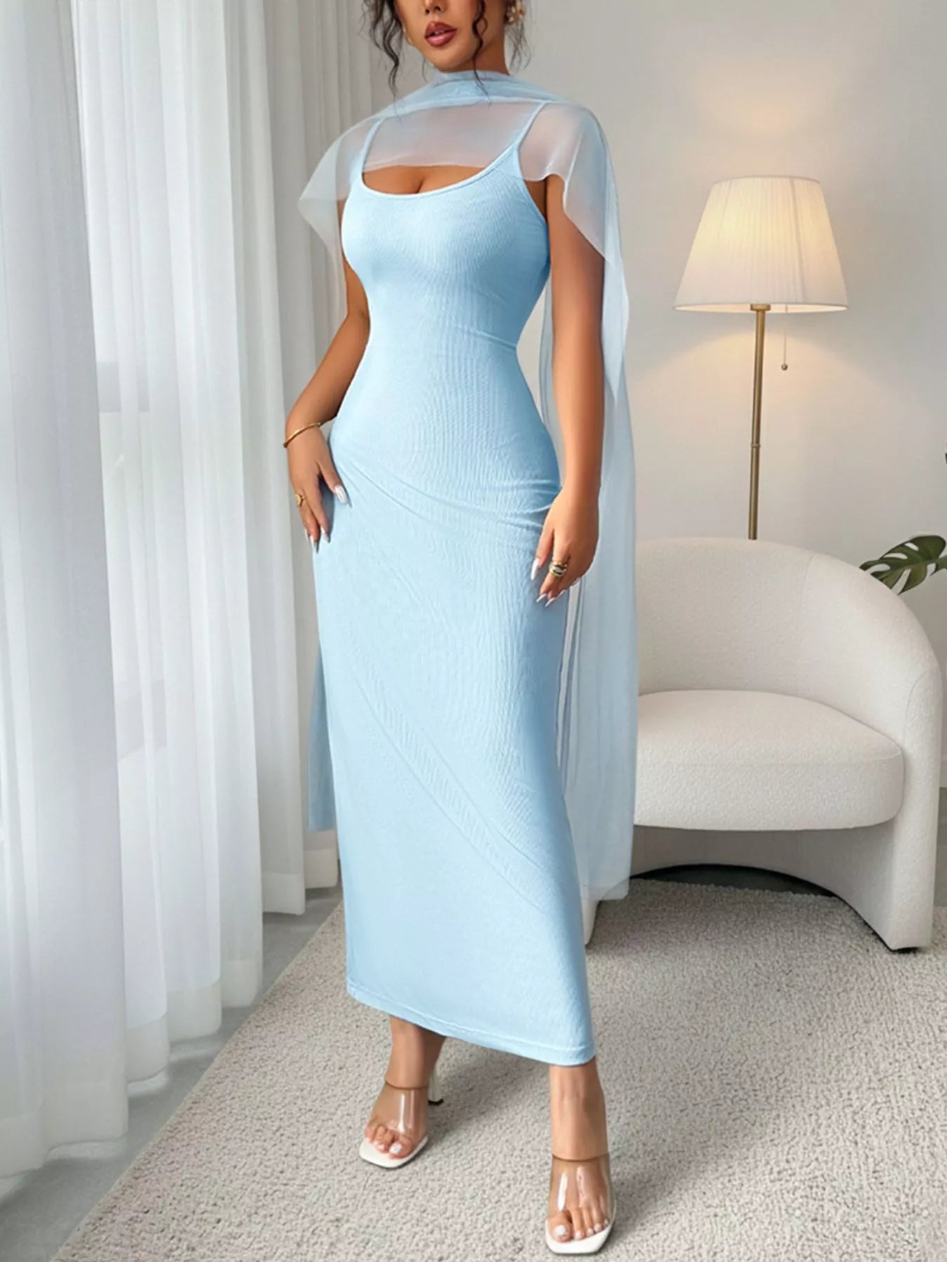 Woman wearing a light blue dress with sheer sleeves in a room with white curtains and a lamp.