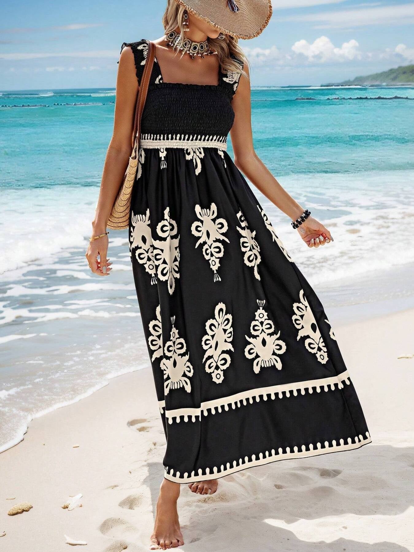Woman in a black dress with white patterns standing on a beach.