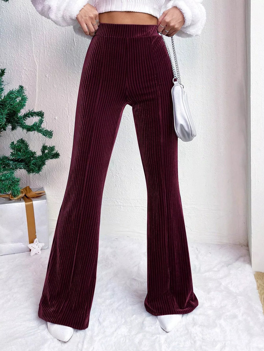 Person wearing burgundy velvet pants with a white top and white shoes, holding a silver handbag.