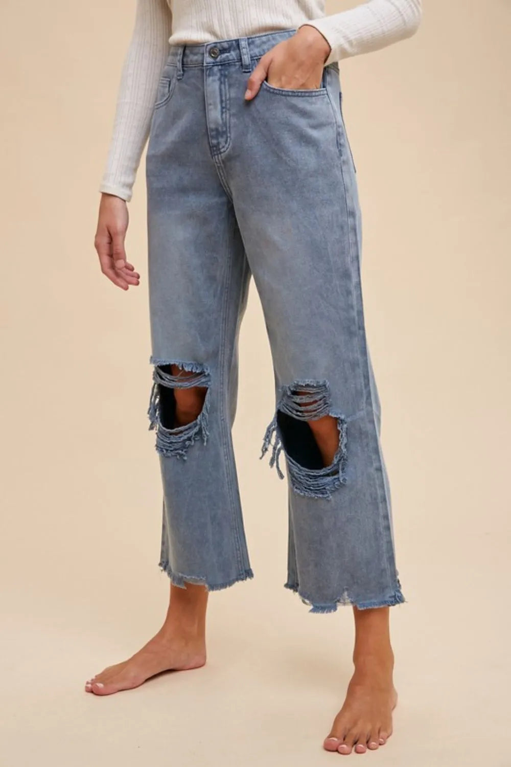 Ripped jeans worn by a person on a beige background