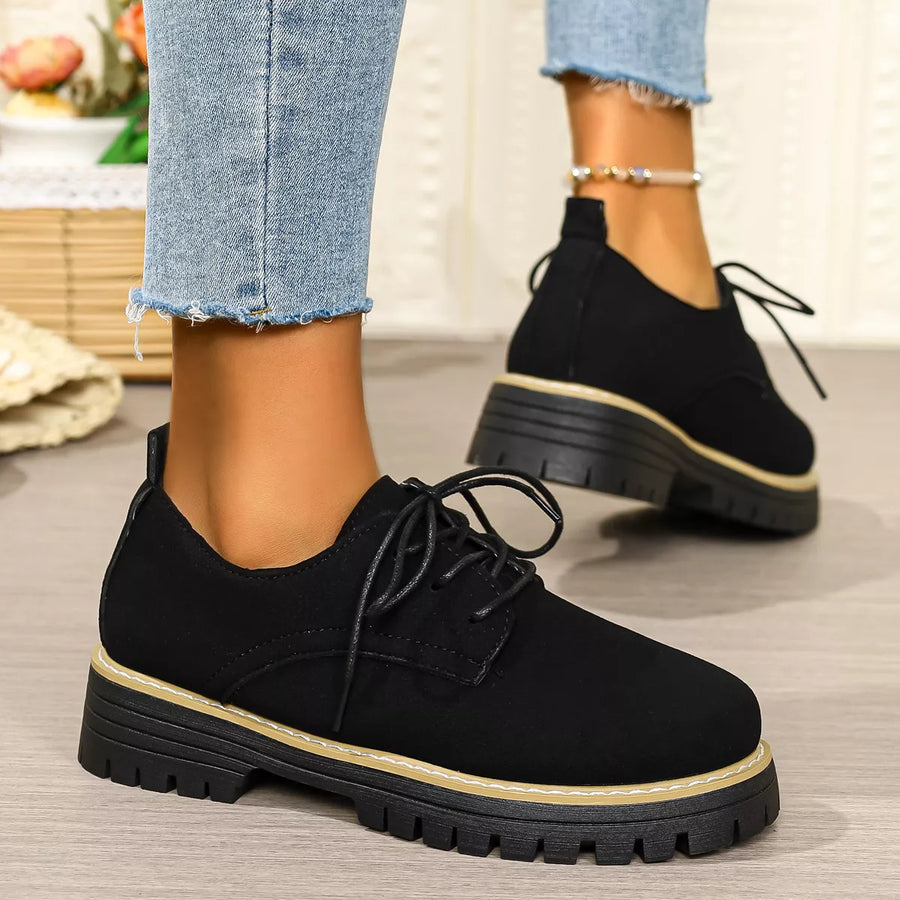 Black lace-up shoes worn with light blue jeans on a neutral background