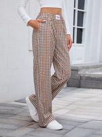 Person wearing brown checkered pants and white sneakers on a stone pavement.