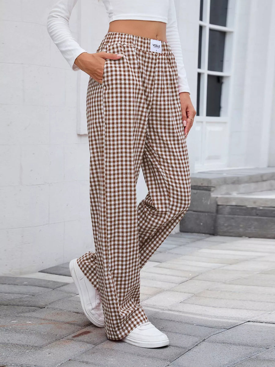 Person wearing brown checkered pants and white sneakers on a stone pavement.