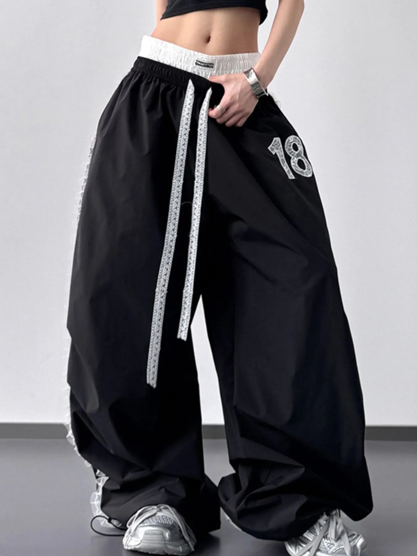 Black baggy pants with white drawstring and number '18' on a plain background
