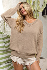 Woman wearing a beige sweater and white shorts in an outdoor setting with a cactus plant.