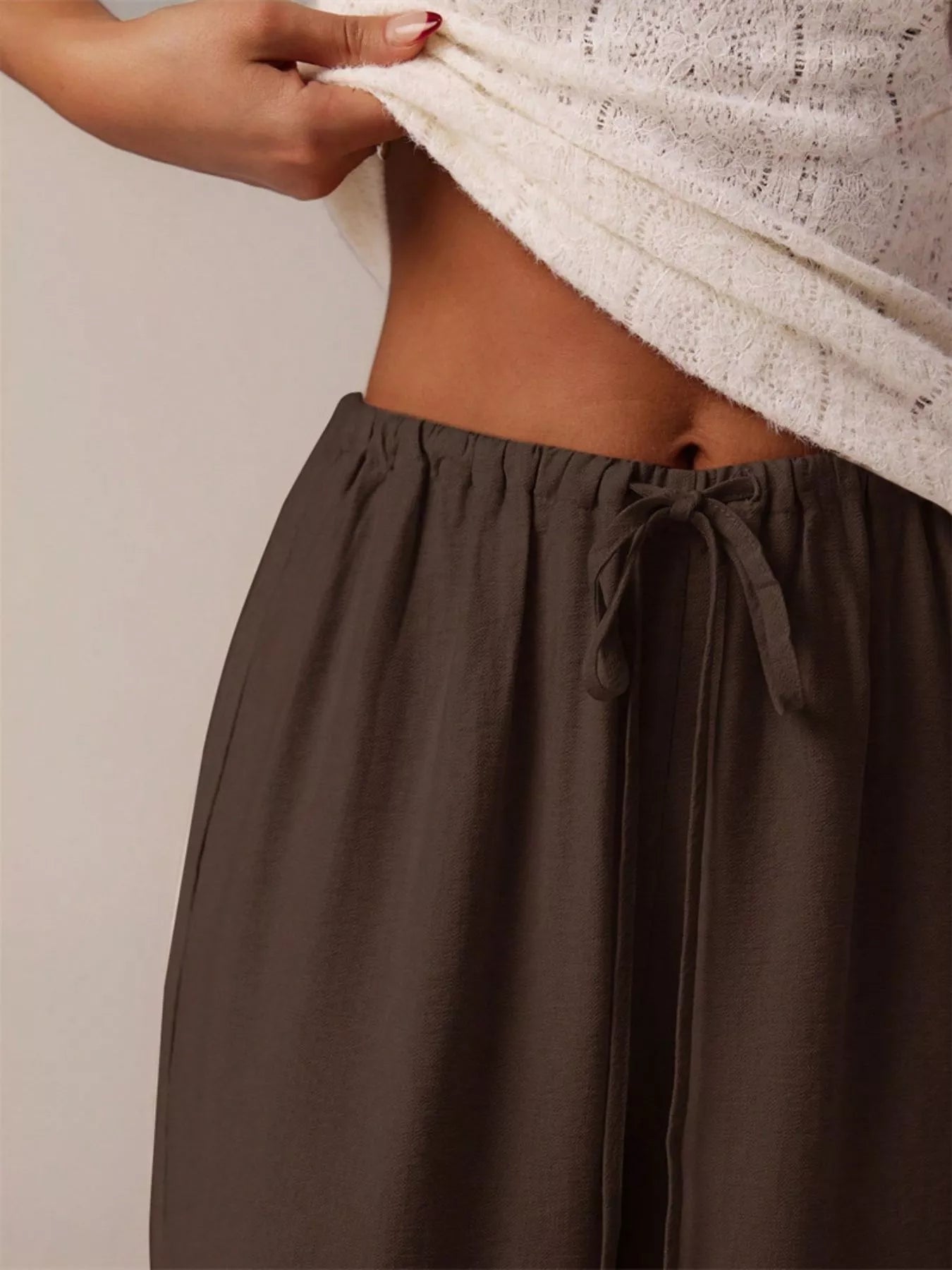 Brown pants with a white lace top on a plain background