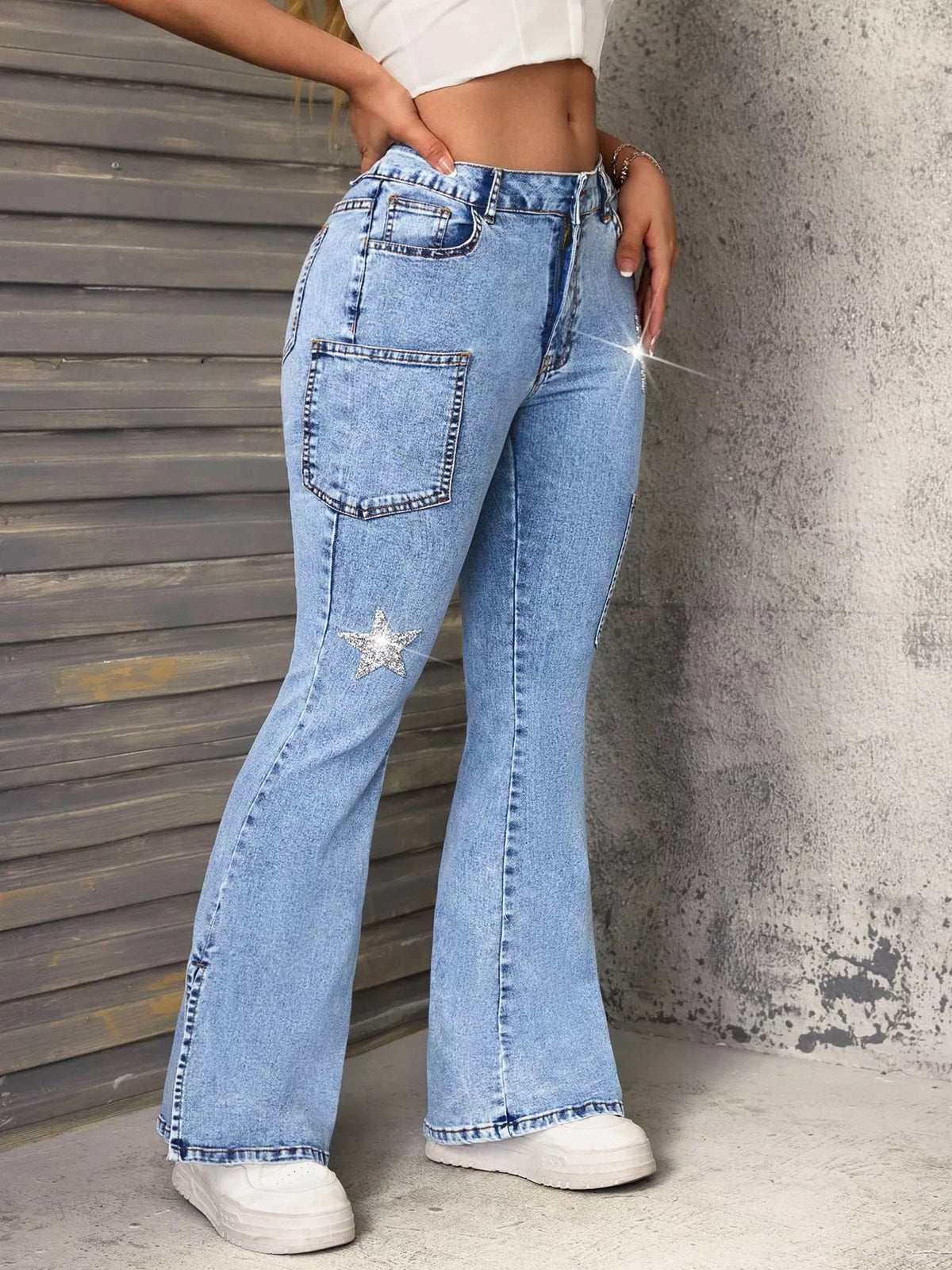 Person wearing light blue flared jeans with a star embellishment against a textured wall.