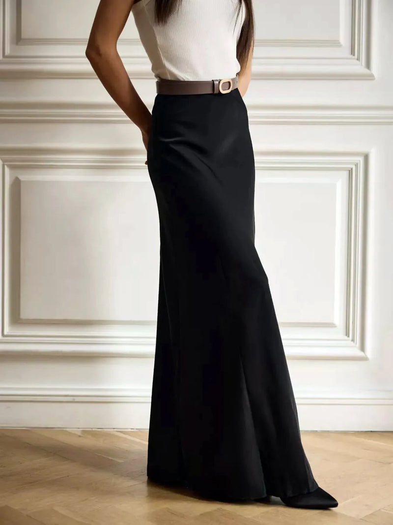 Person wearing a black skirt and white top against a white paneled wall.