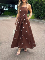 Woman wearing a brown dress with white polka dots standing on a street.