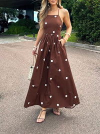 Woman wearing a brown dress with white polka dots standing on a street.