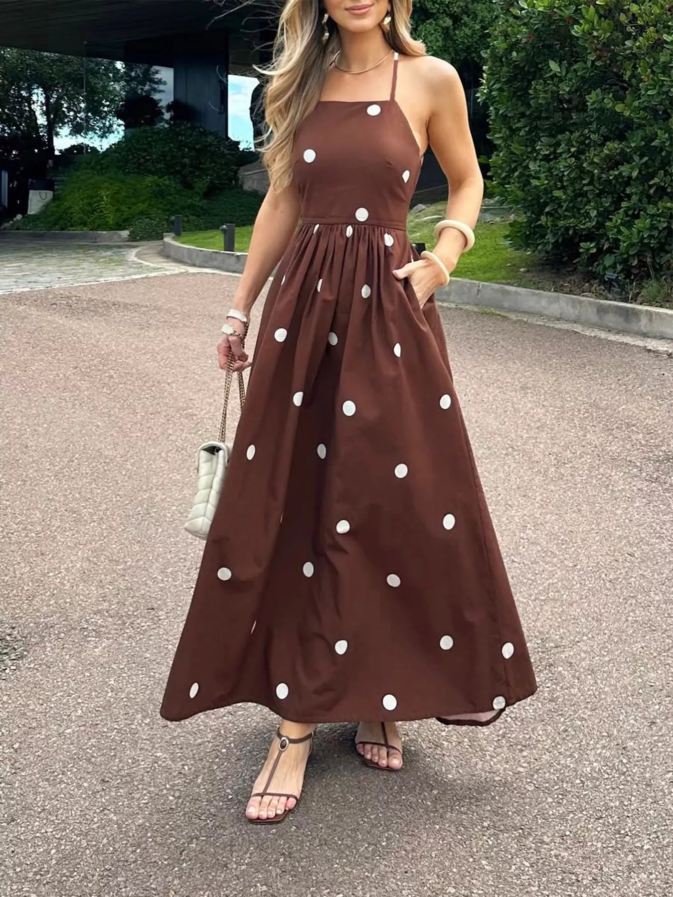 Woman wearing a brown dress with white polka dots standing on a street.