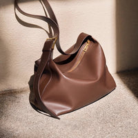 Brown leather handbag with gold zipper on a textured surface