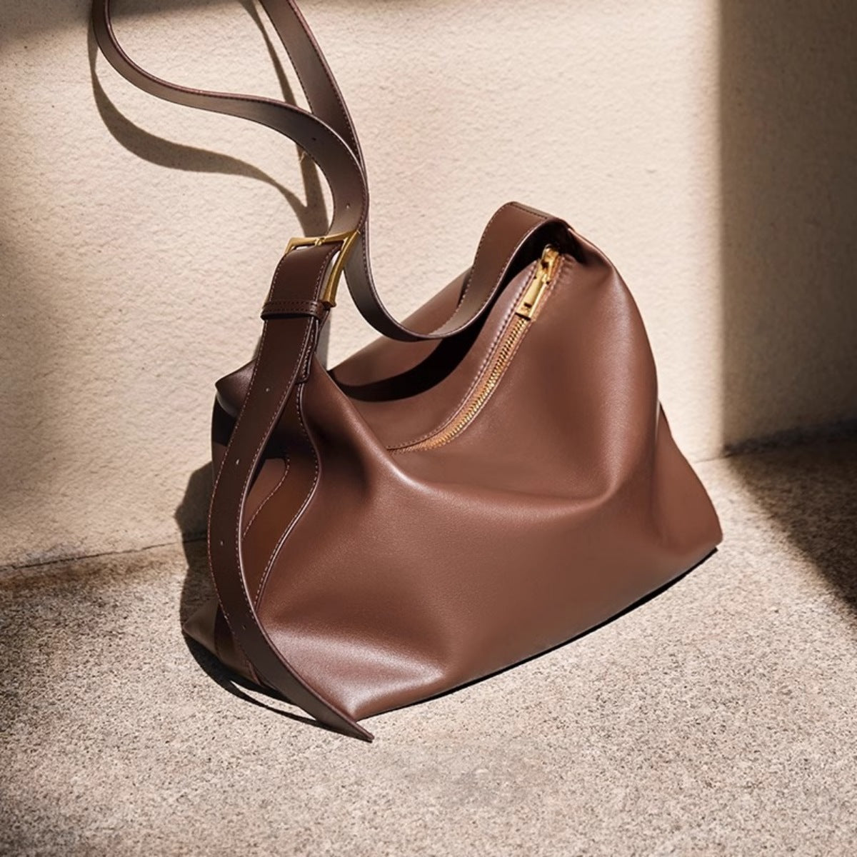 Brown leather handbag with gold zipper on a textured surface