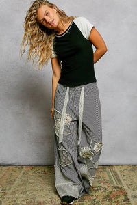 Woman wearing a black and white top with gray distressed pants against a plain background