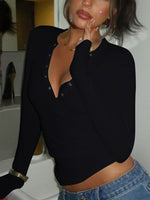 Person wearing a black long-sleeve top with a plunging neckline and blue jeans indoors.