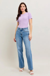 Woman wearing a purple top and blue jeans against a white background