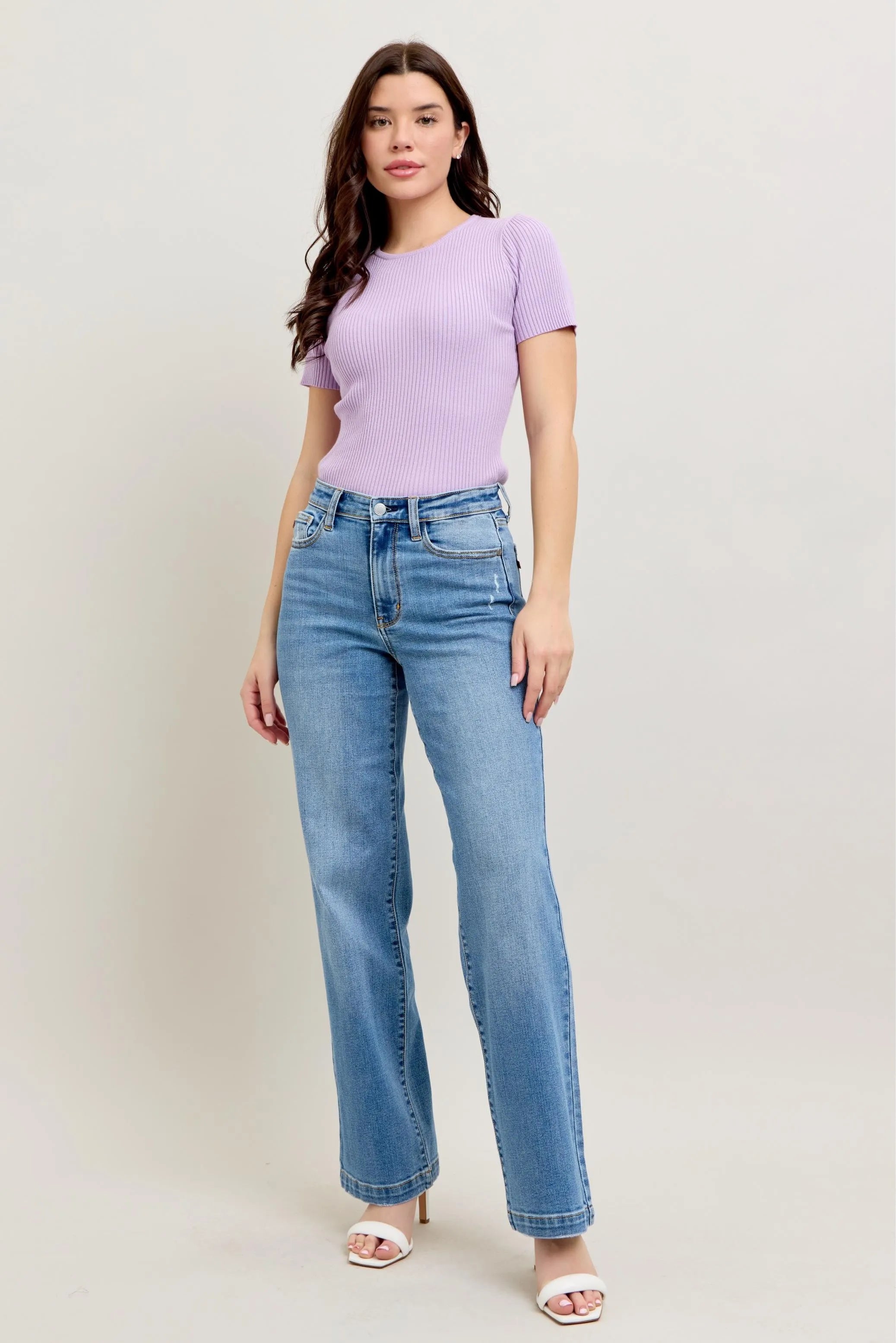 Woman wearing a purple top and blue jeans against a white background